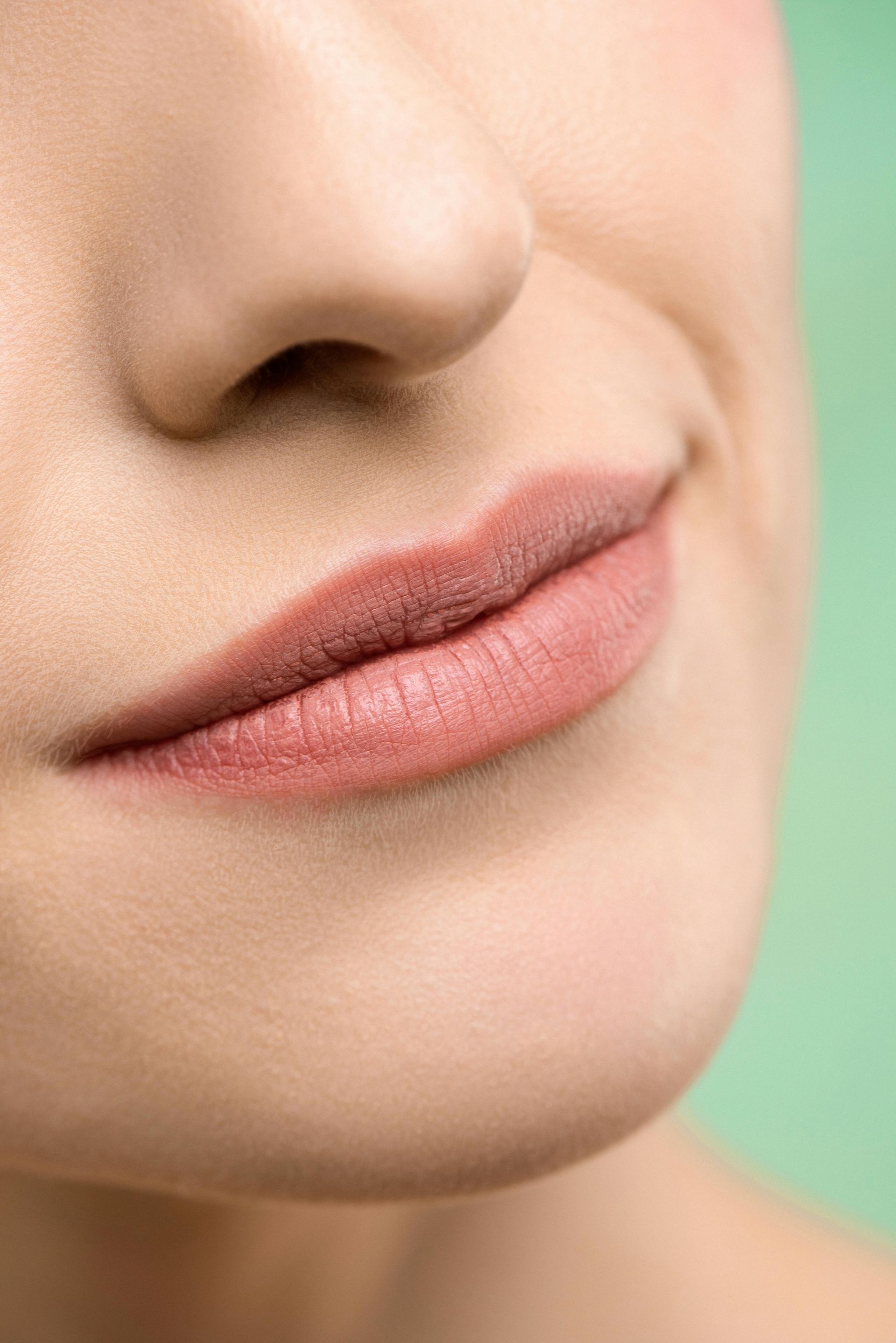 Close-up of a person's face; lips are painted a muted pink, soft smile, light skin.