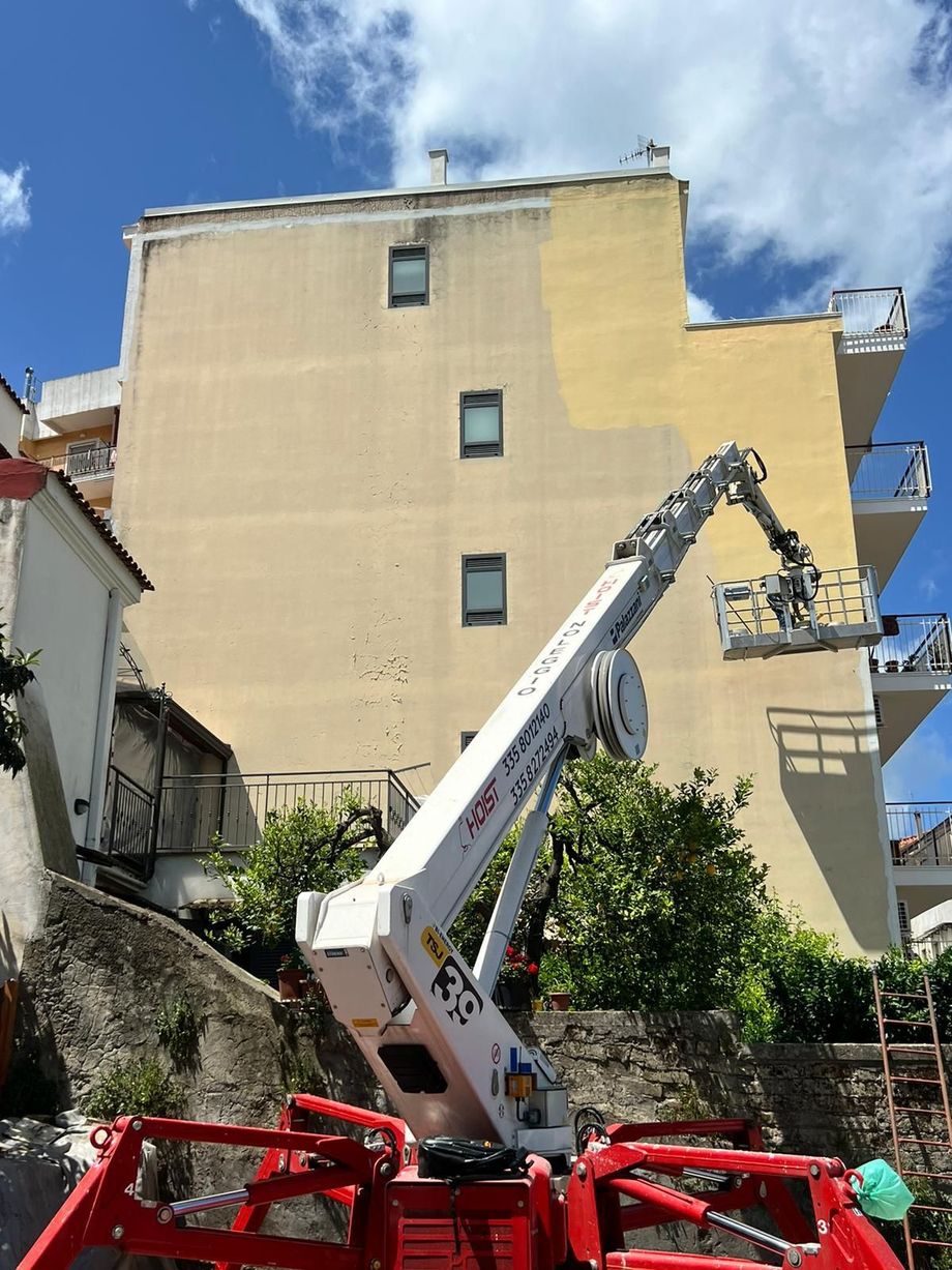 Soggiorno moderno con divano componibile beige, TV a parete, mensole e ampia finestra con tende.
