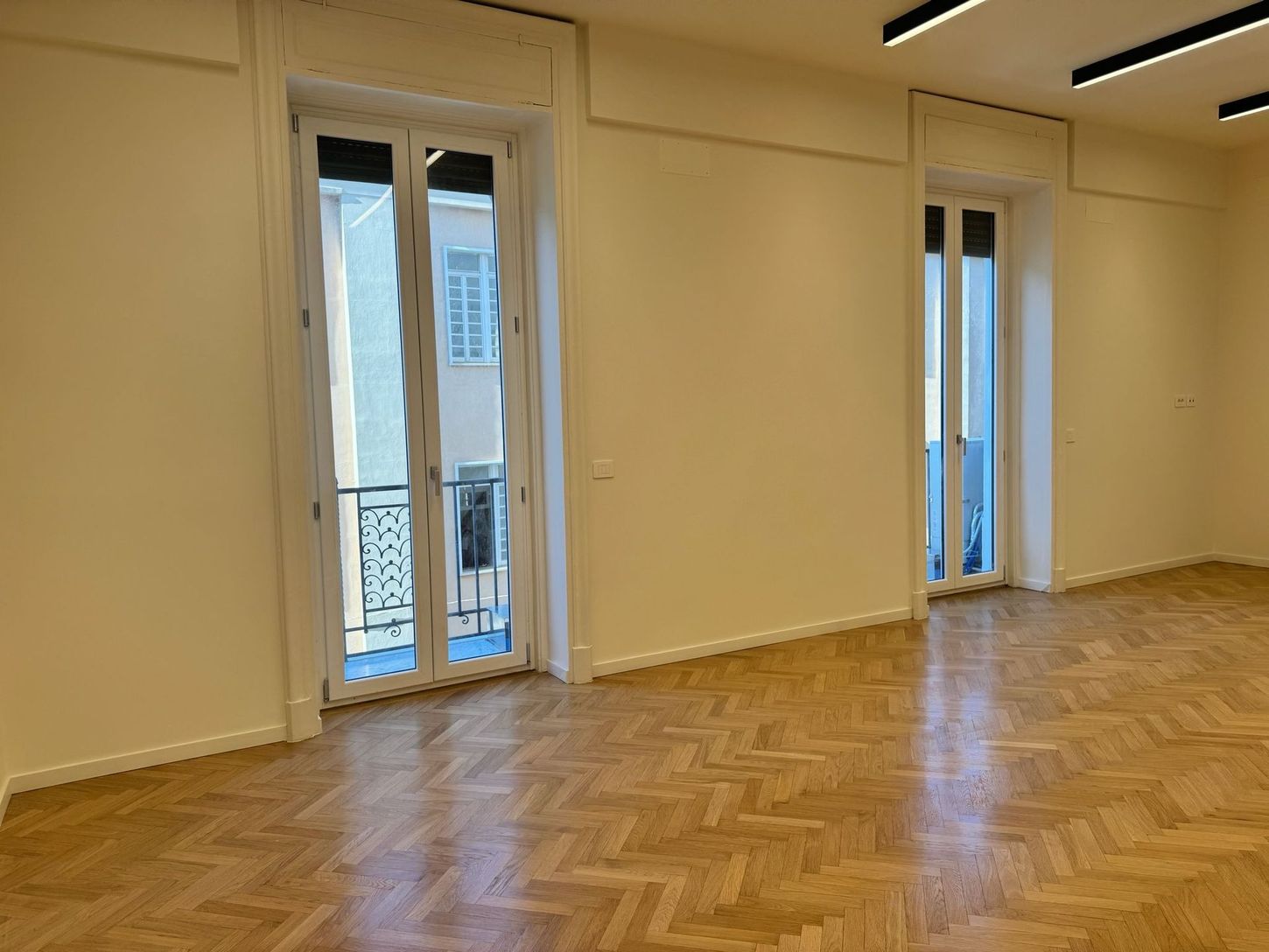 Soggiorno moderno con divano componibile beige, TV a parete, mensole e ampia finestra con tende.