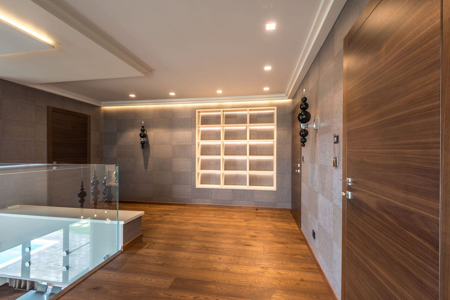 Soggiorno moderno con divano componibile beige, TV a parete, mensole e ampia finestra con tende.