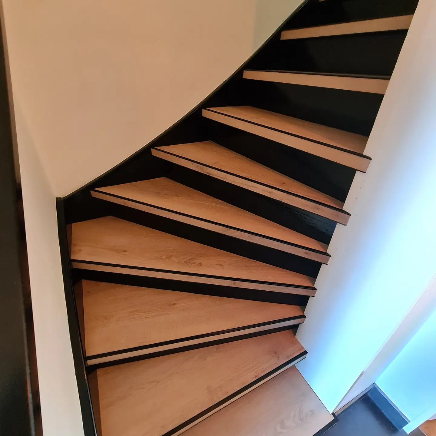 Een wenteltrap met houten treden en zwarte leuning