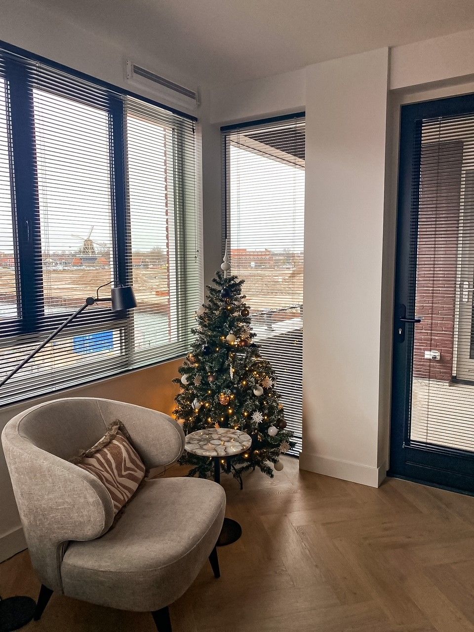 Een woonkamer met een stoel en een kerstboom voor het raam.