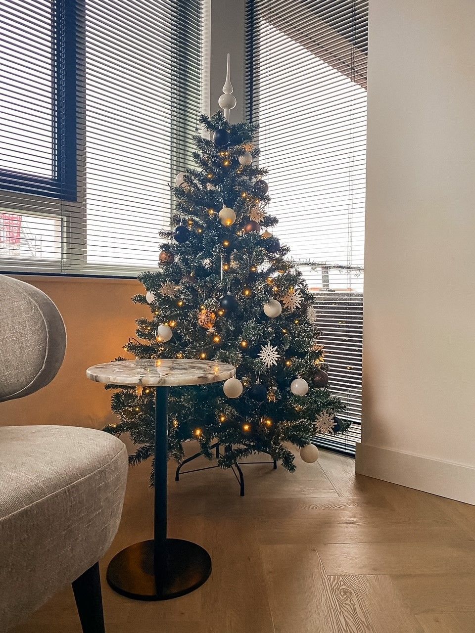 Een kerstboom staat op een tafel naast een stoel in de woonkamer.
