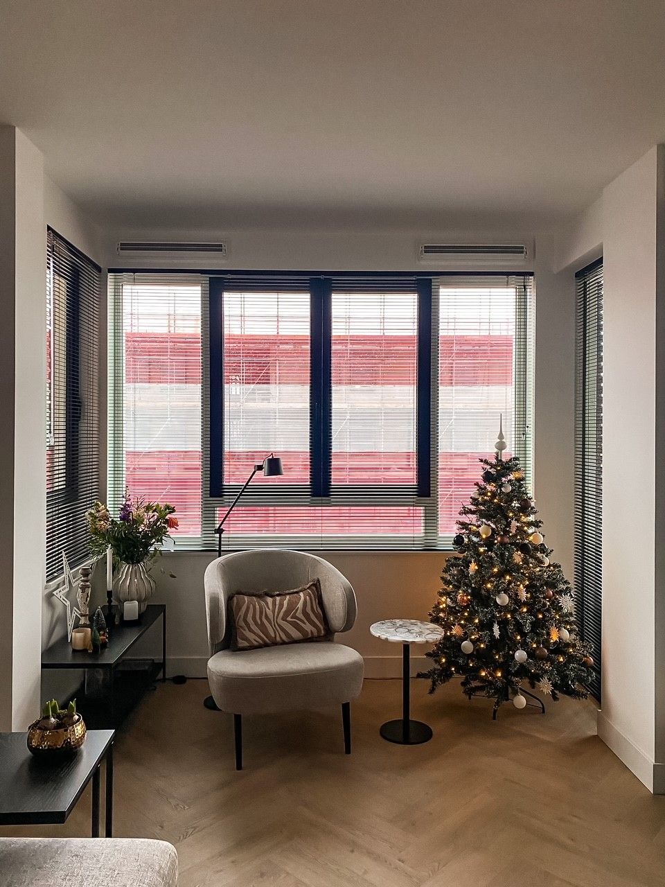 Een woonkamer met een stoel en een kerstboom voor het raam.