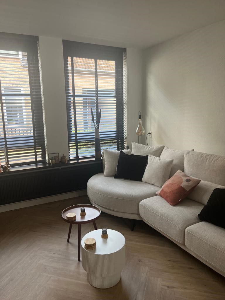 Een woonkamer met een bank, twee tafels en een raam.