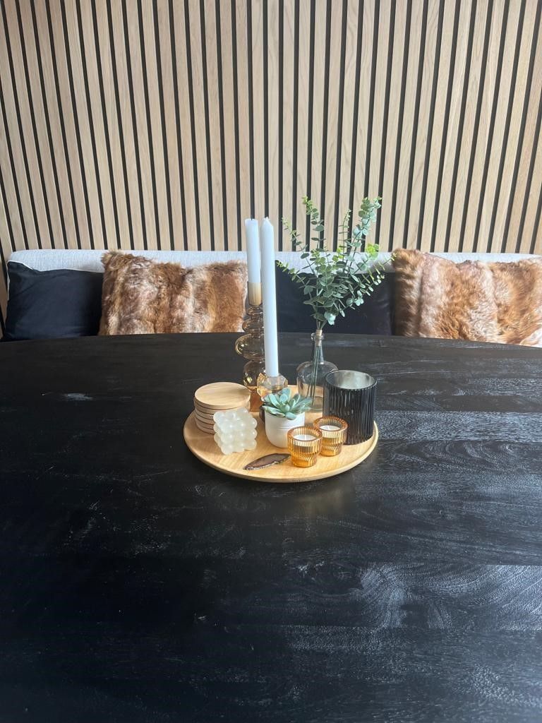 Een zwarte tafel met daarop een houten dienblad en kaarsen.