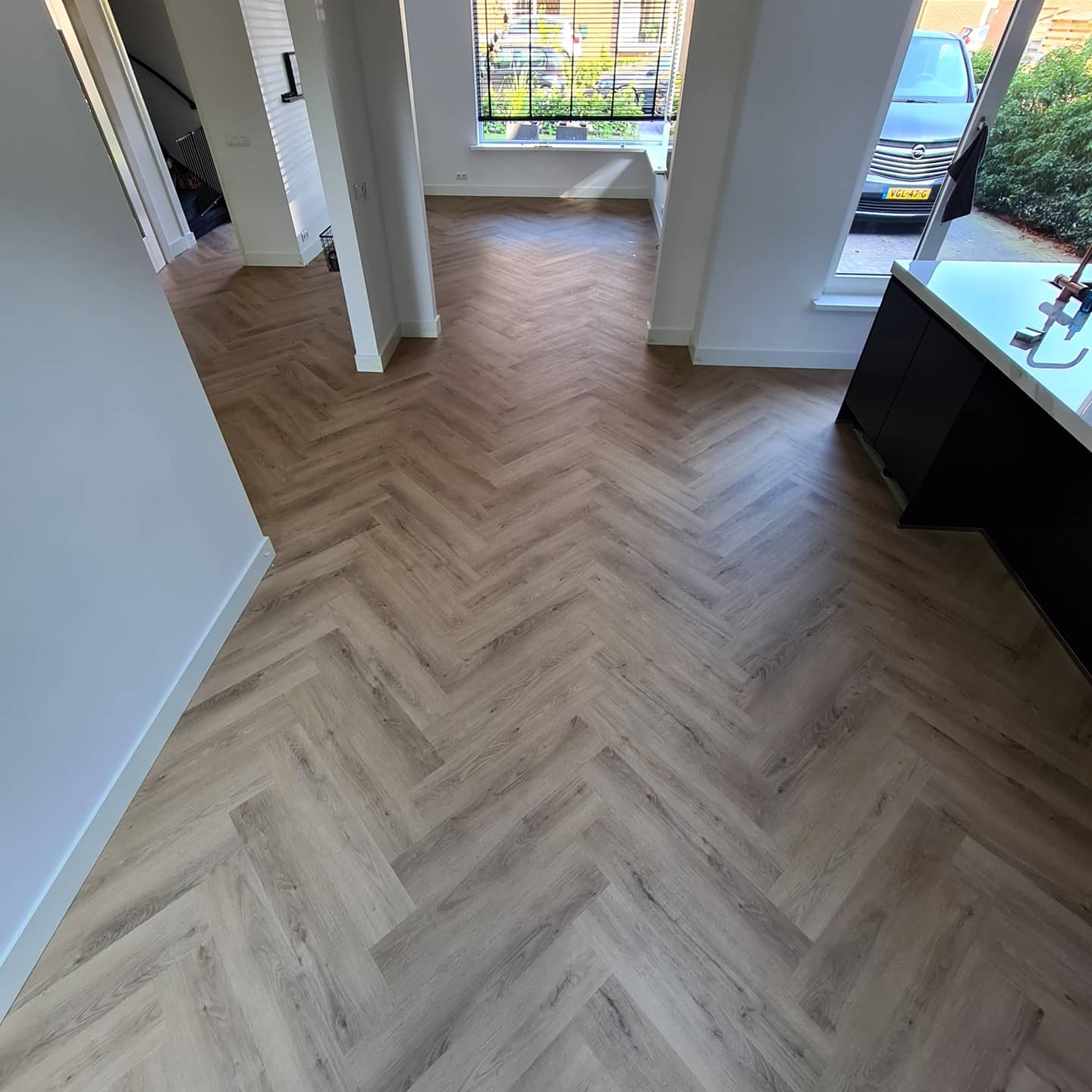 Een visgraatvloer in een woonkamer met op de achtergrond de keuken.