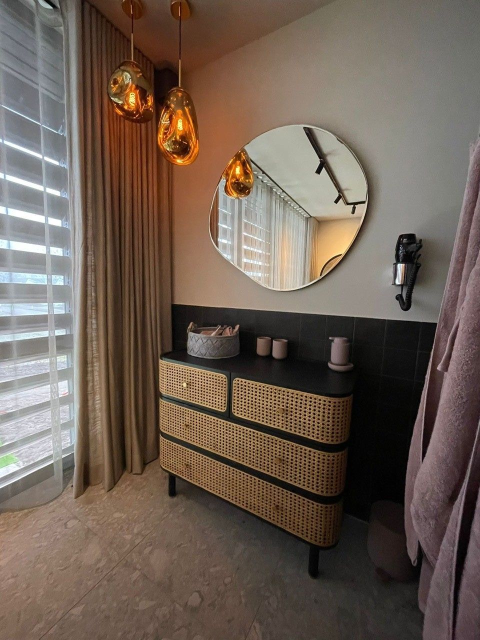 Een badkamer met een rieten ladekast en een ronde spiegel.