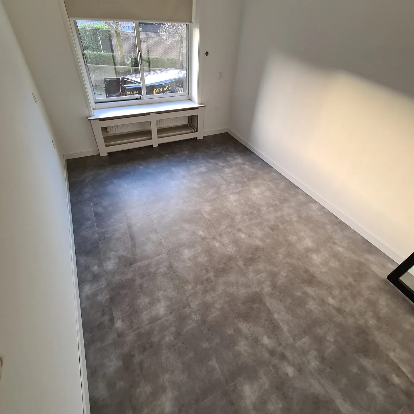 Een kamer met een raam en een grijze vloer.