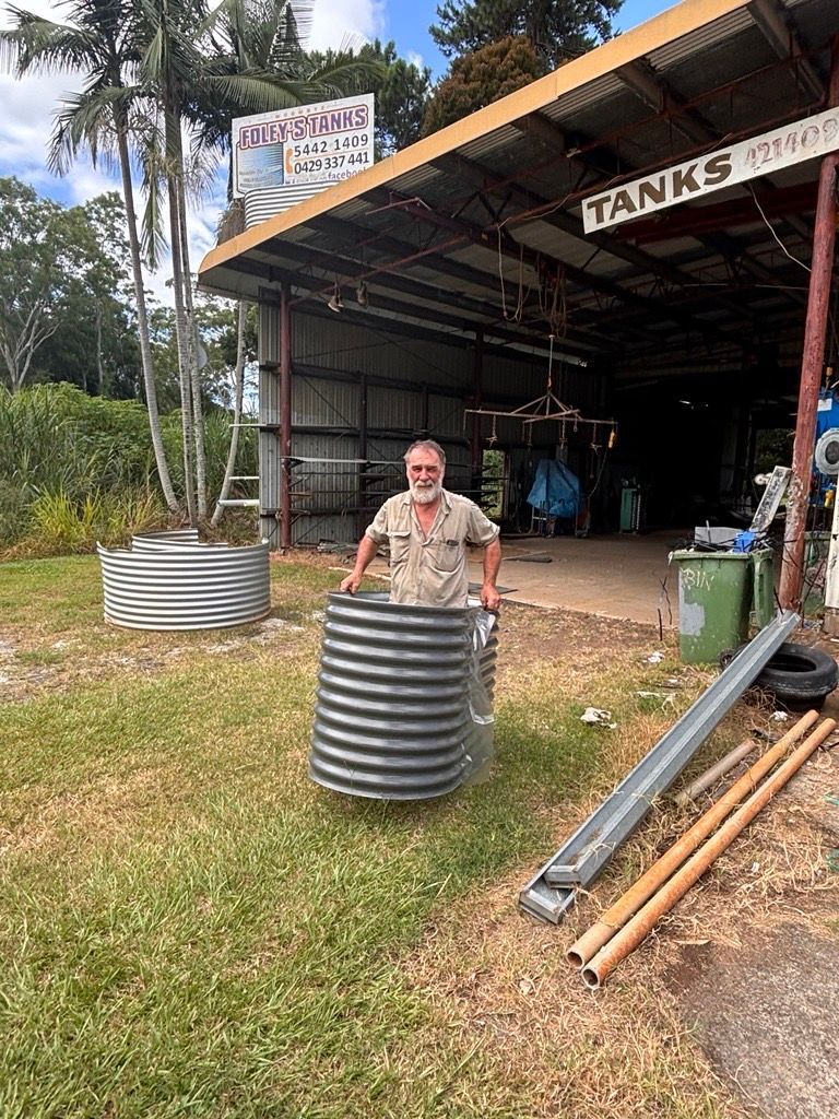 A Man is Standing Next to a Large Metal Tank in Front of a Building — Foley's Tanks in Woombye, QLD