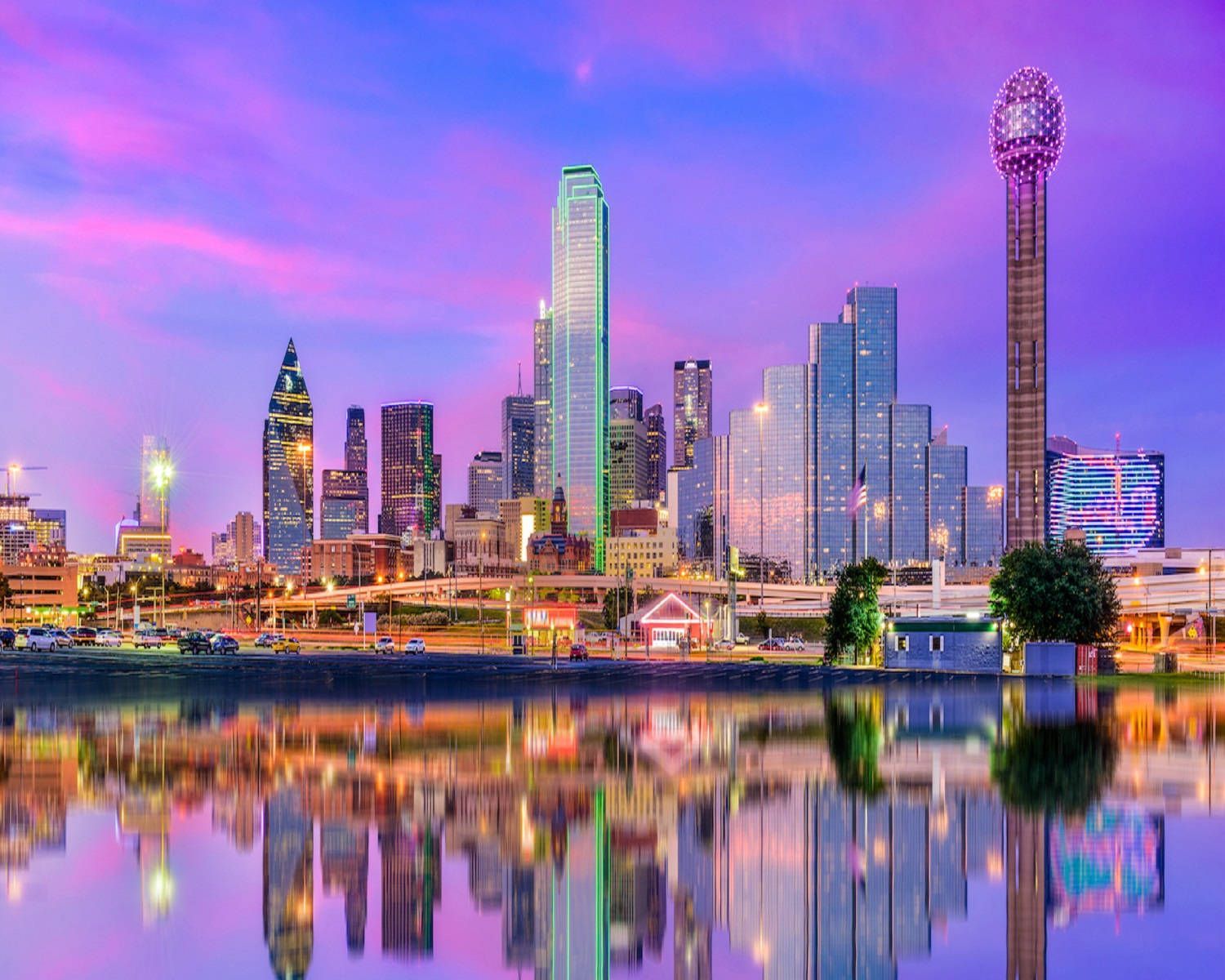 Dallas, Texas skyline at dusk reflecting in calm water; purple and blue sky.