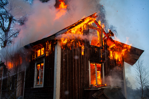 House engulfed in flames, with smoke and fire pouring from the roof and windows.