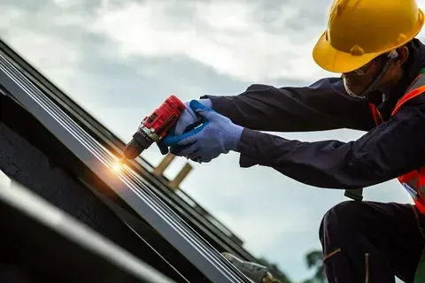 Worker in yellow hard hat welding metal on a rooftop, with bright sparks flying.