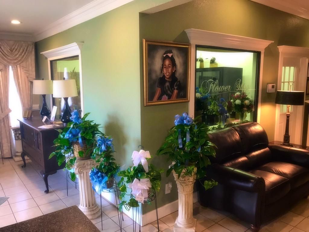 An elegant entryway with green walls, a portrait, a dark leather sofa, and floral arrangements on pedestals.
