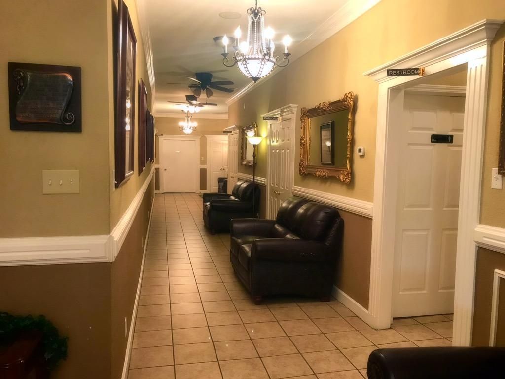 A view of a long hallway with light tile floors, brown walls, chandeliers, and black leather seating.