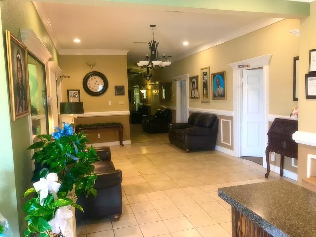 A furnished reception area with tiled floors, dark leather armchairs, wall art, a ceiling chandelier, and a potted plant.