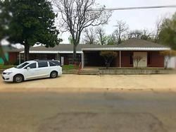A white minivan is parked on a gravel lot in front of a low, single-story red brick commercial building with a porch.