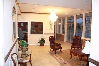 A bright office lobby with tile floors, two brown leather chairs, a glass coffee table, and a crystal chandelier.