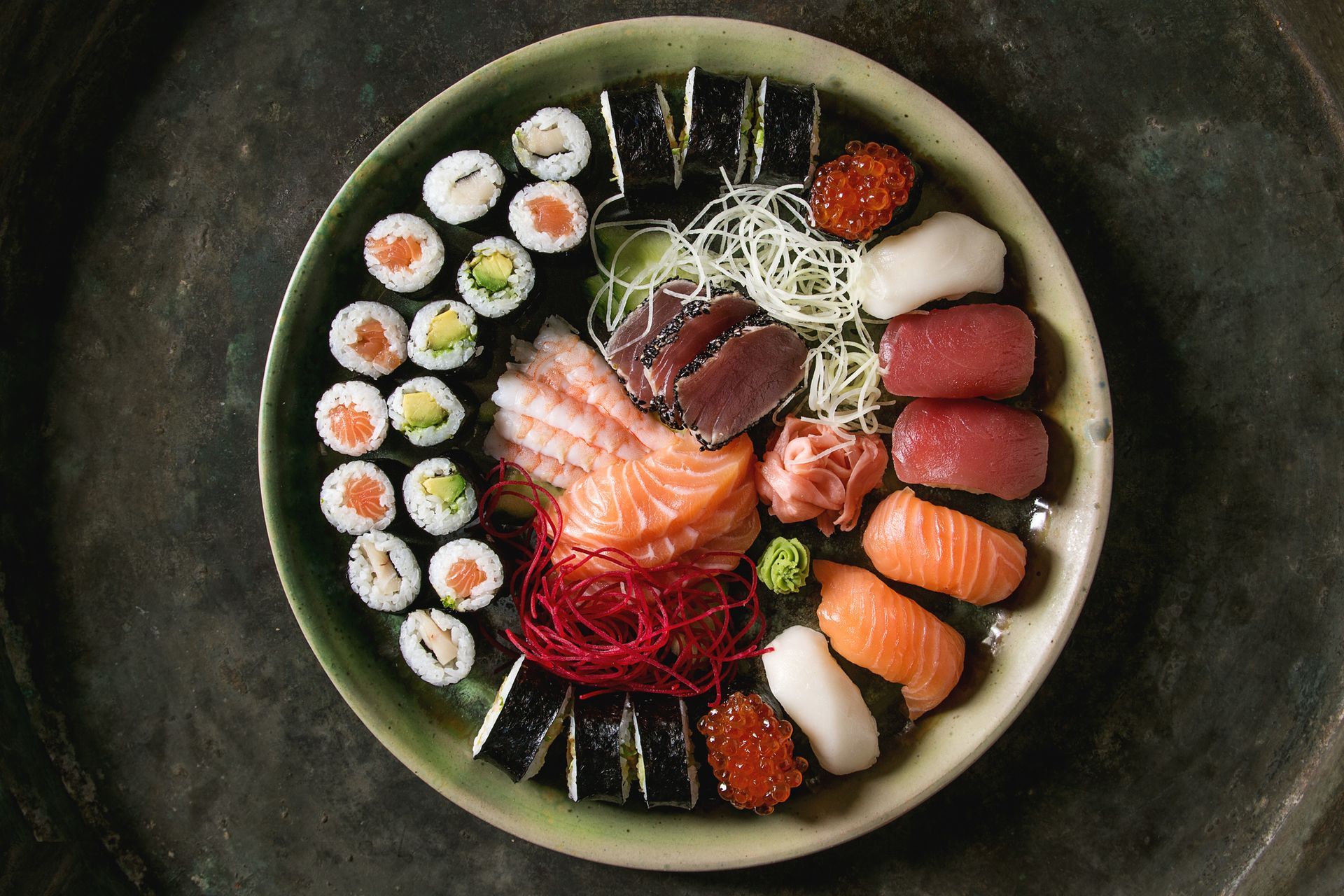 Sushi e sashimi colorati disposti in una ciotola rotonda su un tavolo scuro