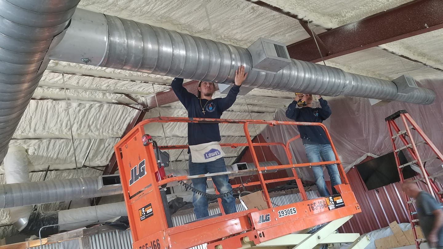 Two workers on an orange scissor lift install metal HVAC ductwork on the ceiling of a construction site. Two workers on an orange scissor lift install metal HVAC ductwork on the ceiling of a construction site.