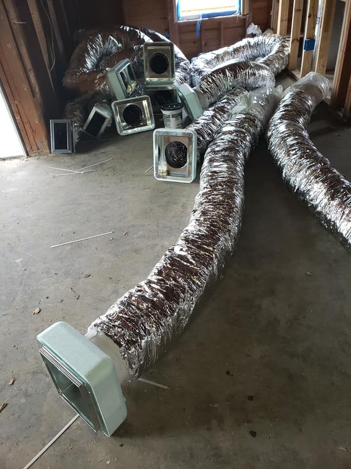 Flexible insulated silver HVAC ductwork sections with plastic vent boots scattered on an unfinished construction floor.