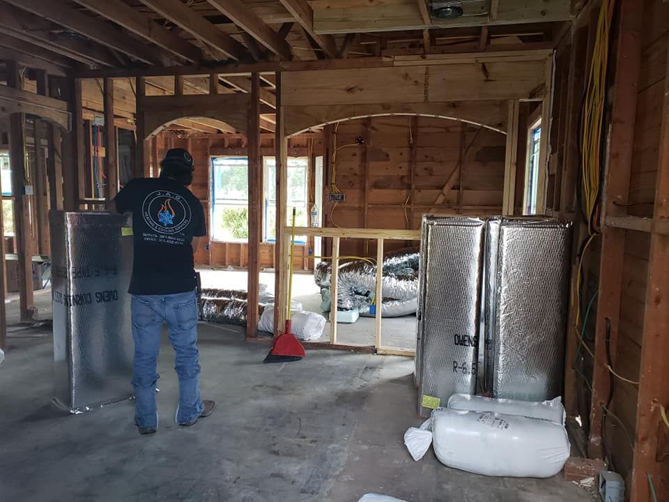 A person stands in a home under construction, surrounded by wall framing, insulation, and large metallic ductwork. A person stands in a home under construction, surrounded by wall framing, insulation, and large metallic ductwork.
