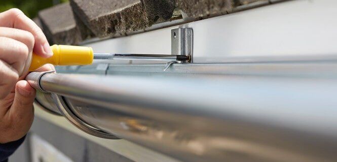 A person is fixing a gutter with a screwdriver.