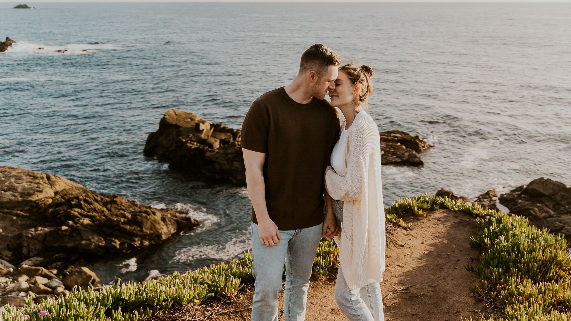 A man and a woman are standing next to each other on a cliff overlooking the ocean.