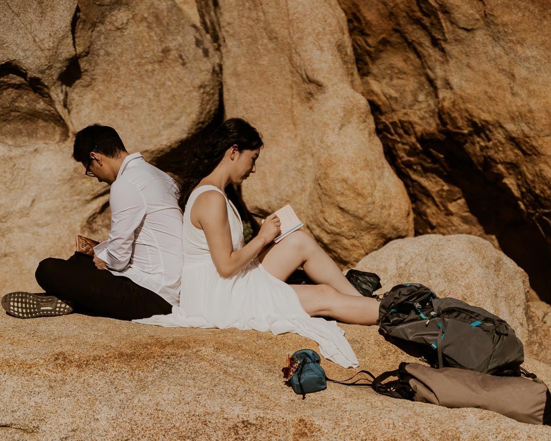 A man and a woman are sitting back to back on a rock.