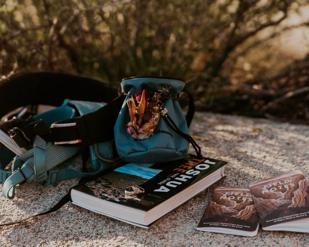 A backpack , books , and a blue bag are sitting on a rock.