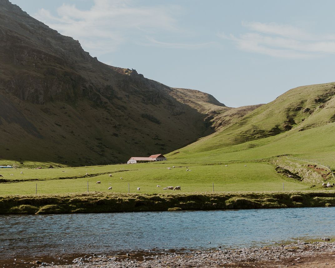 A lake in the middle of a grassy field with mountains in the background