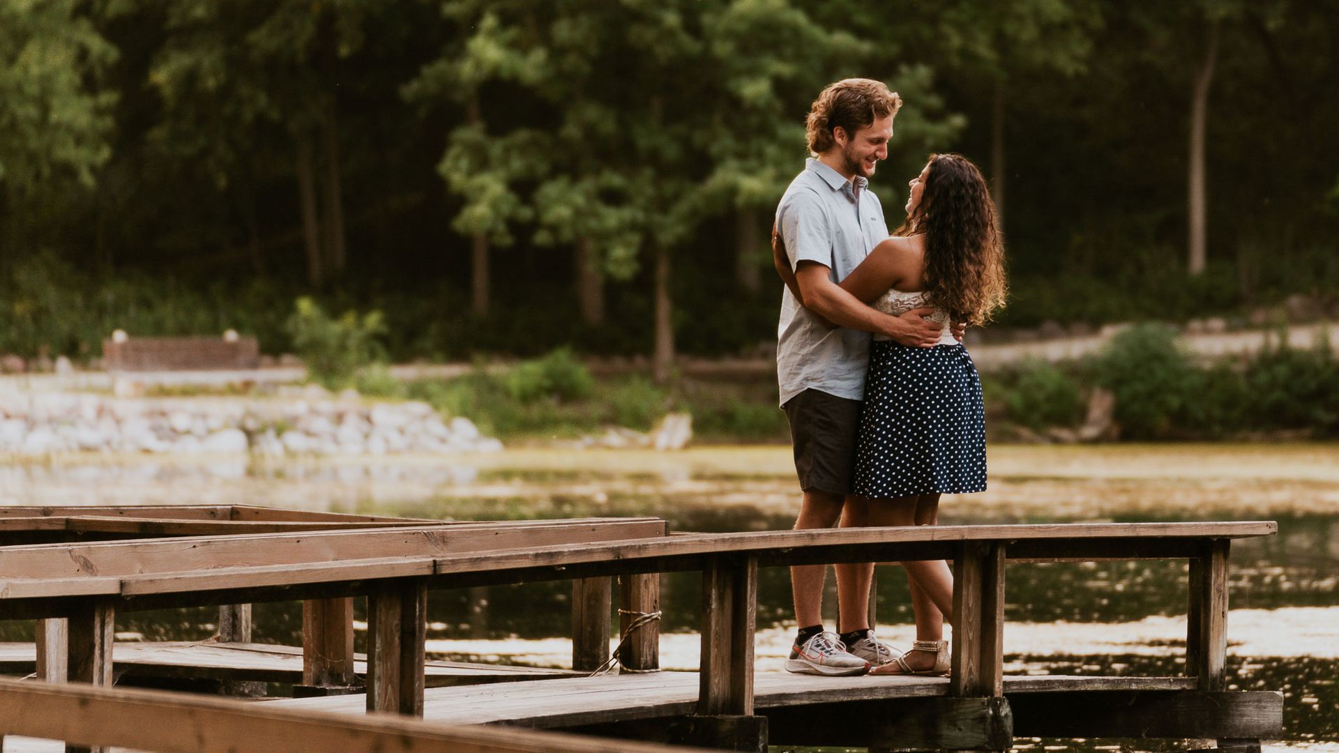 A man and a woman are standing on a wooden dock overlooking a lake.