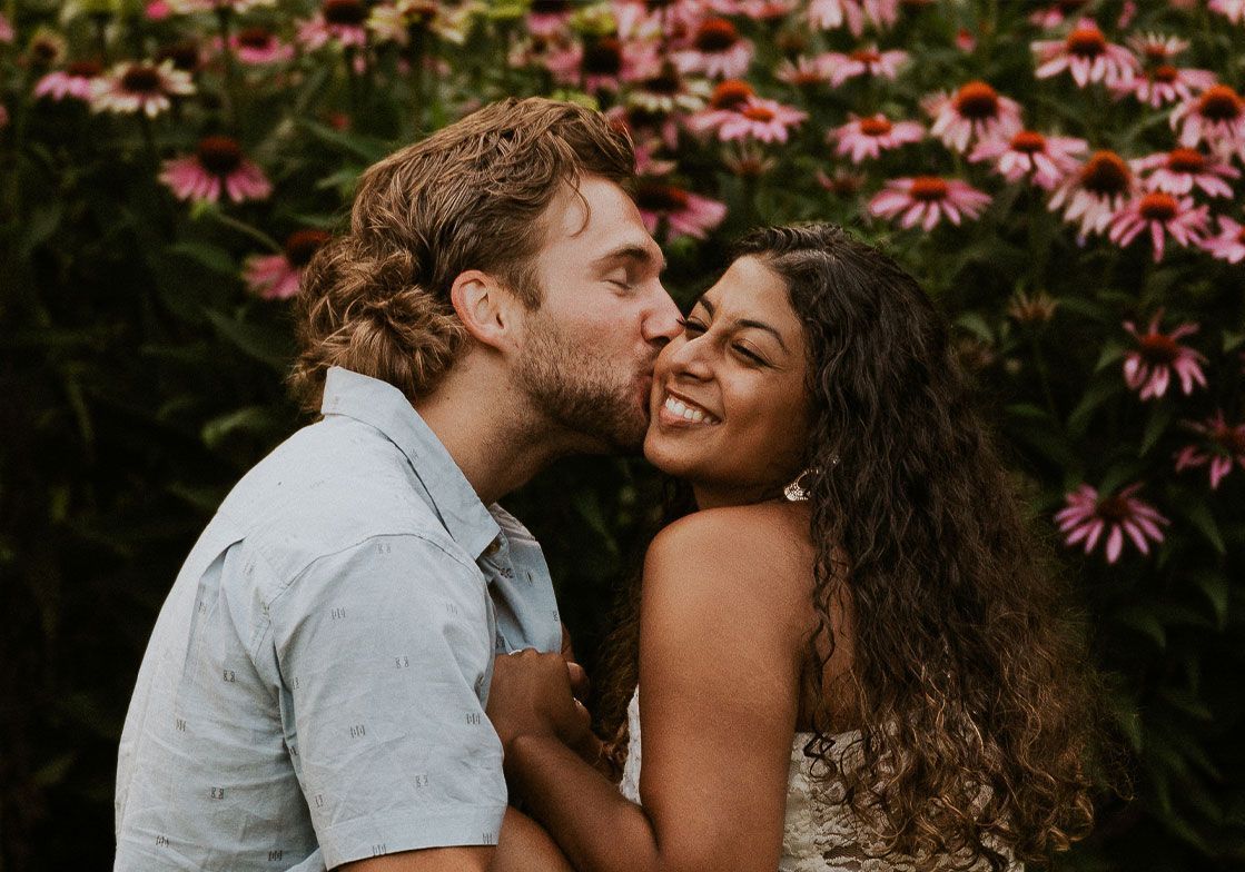 A man is kissing a woman on the cheek in front of flowers.