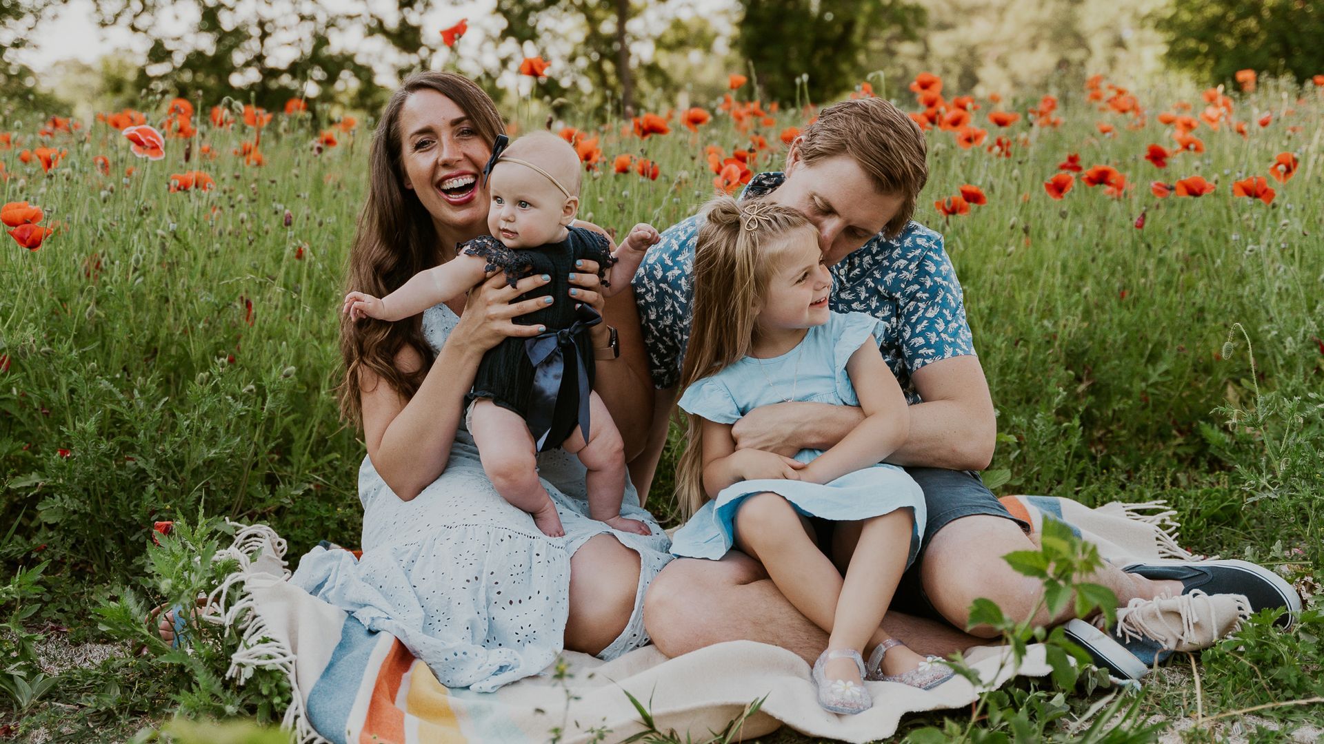 A family is sitting on a blanket in a field of poppies.