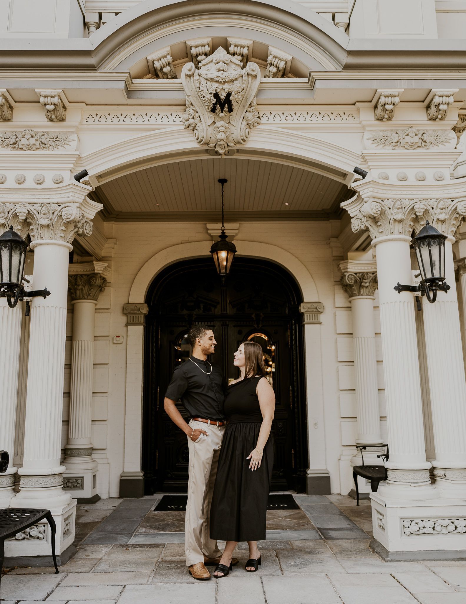 A bride and groom are standing next to each other in front of a window holding a bouquet of flowers.
