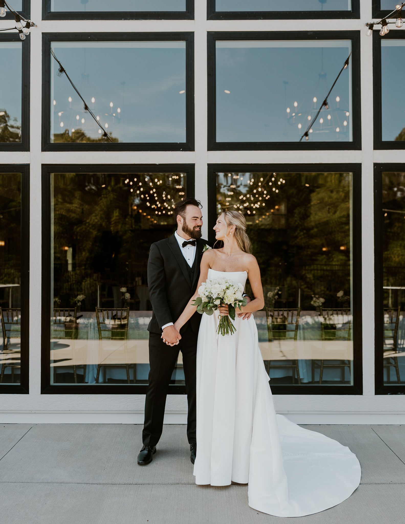 Bride and groom in wedding attire standing outside a modern building with large windows