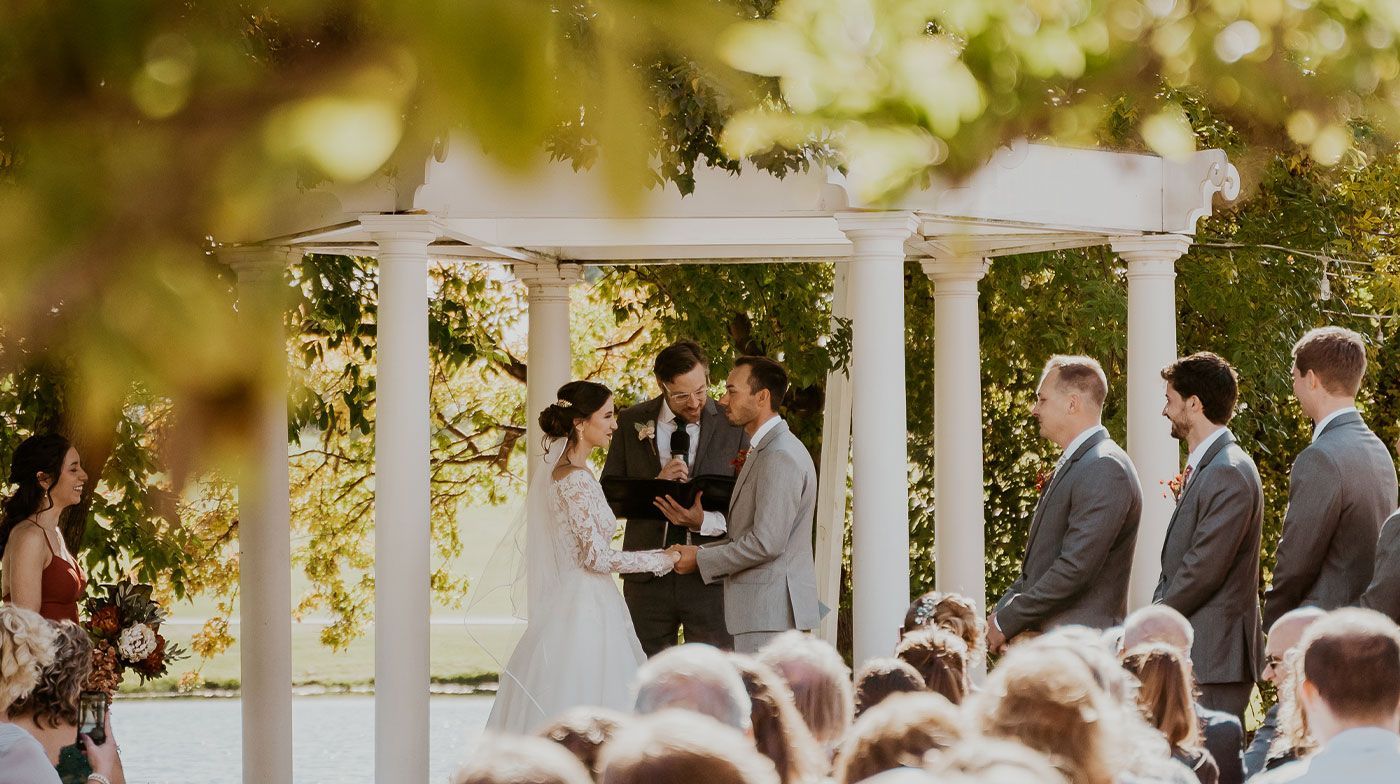 A bride and groom are getting married under a pergola in front of a crowd of people.