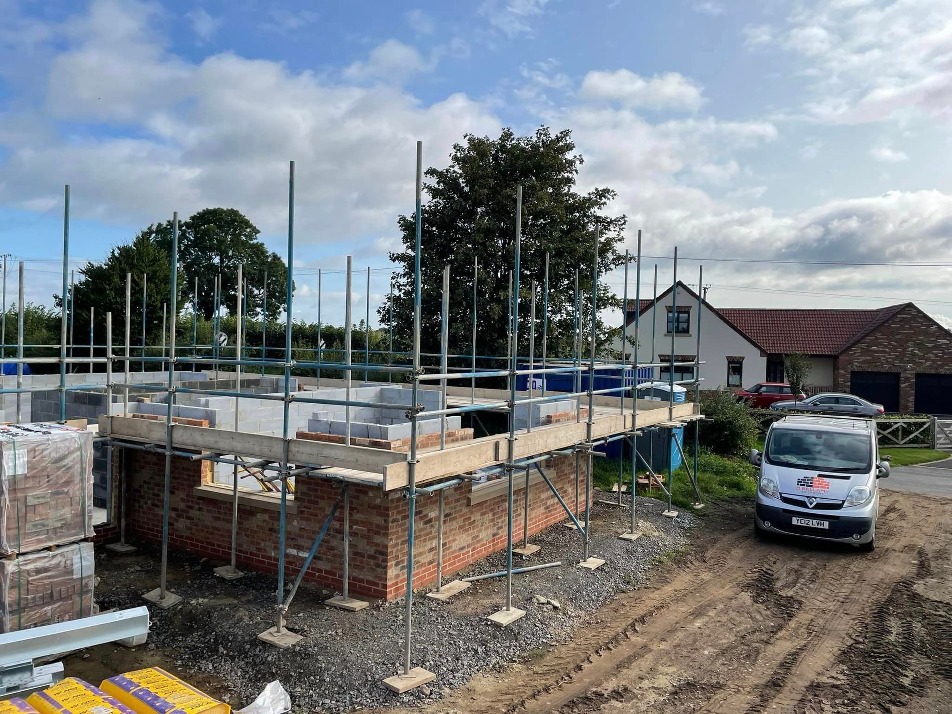 A white van is parked in front of a building under construction.