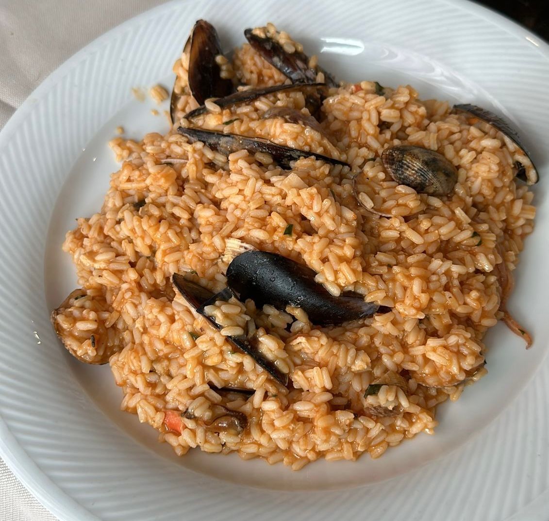 Risotto alle cozze su piatto bianco; salsa all'arancia, riso e gusci di cozze nere.
