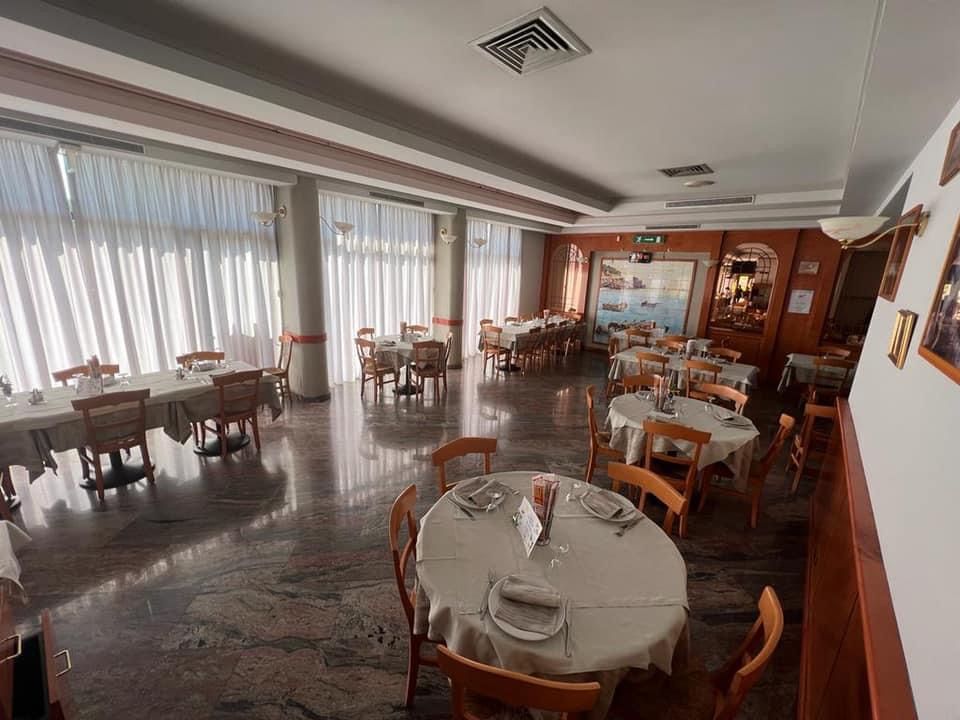 Interno del ristorante con tavoli rotondi e rettangolari, finestre drappeggiate e un pavimento in marmo lucido.