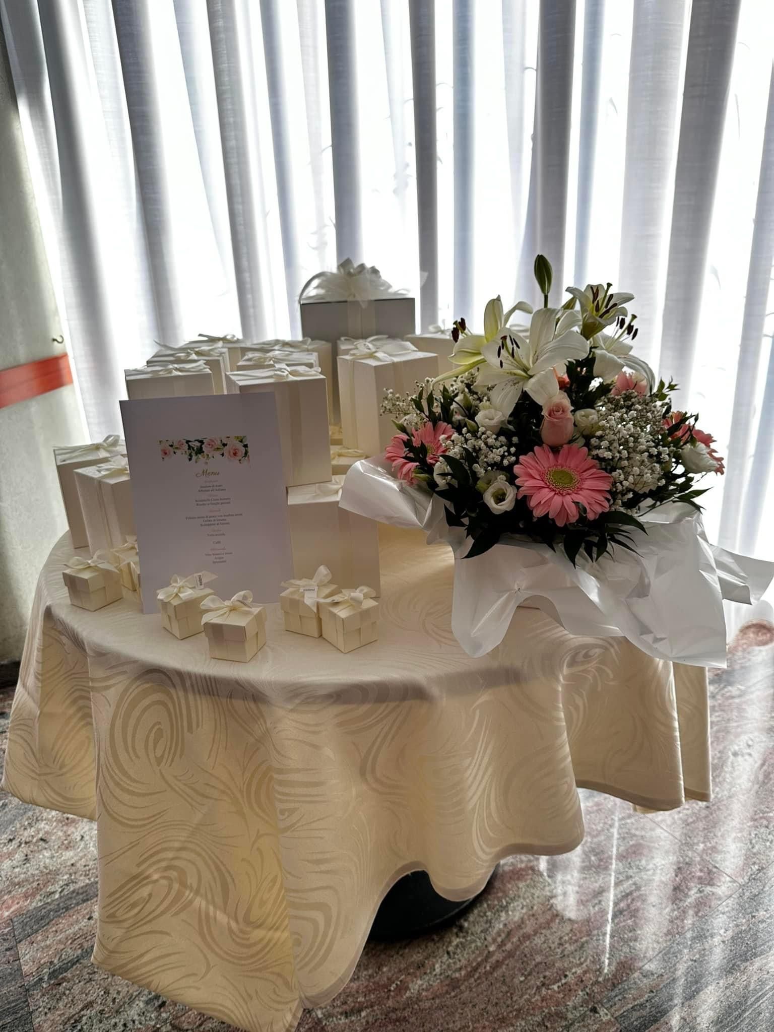 Un tavolo con scatole regalo e una composizione floreale; il tavolo è apparecchiato per un evento.