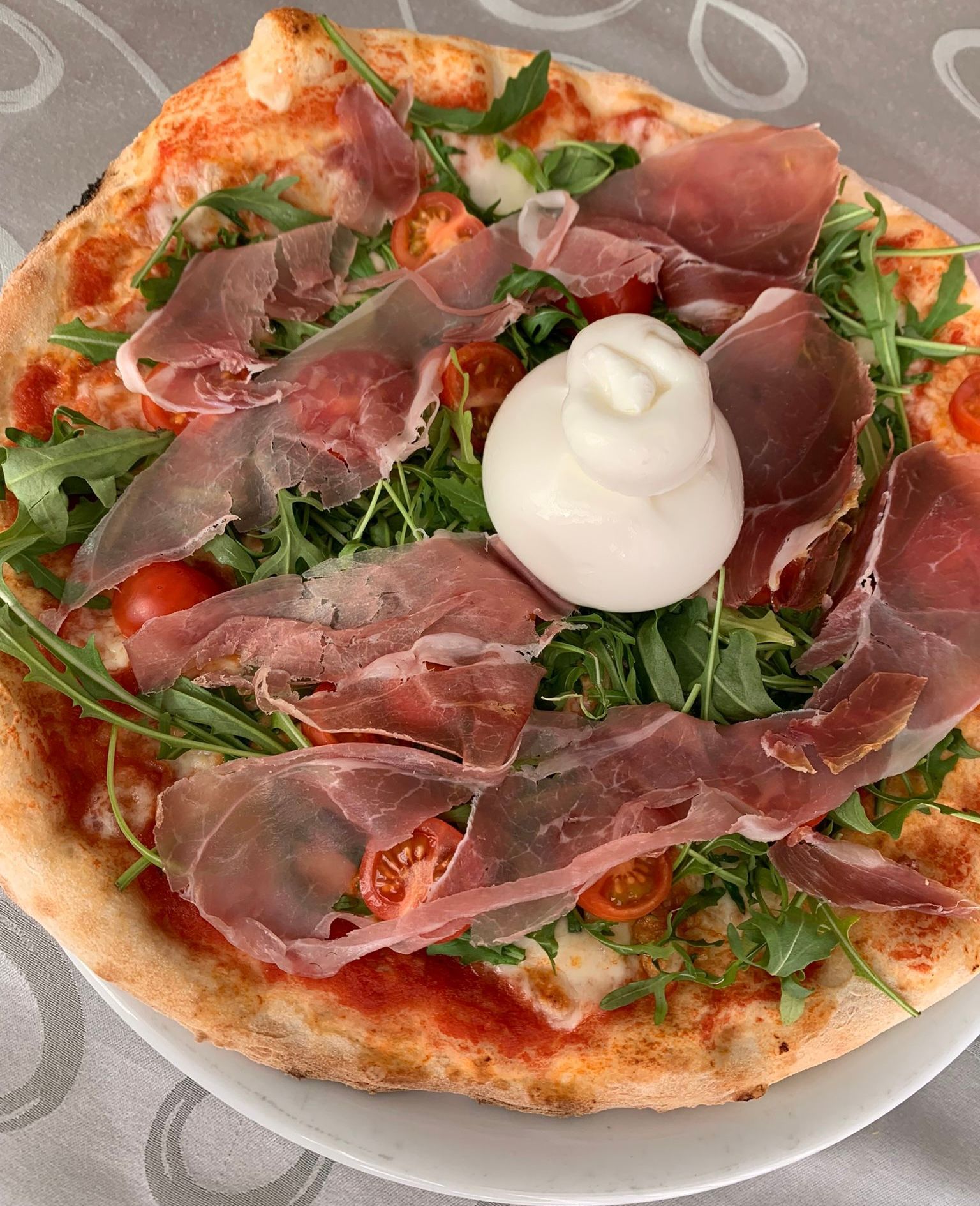 Pizza con prosciutto crudo, rucola, pomodorini e burrata.