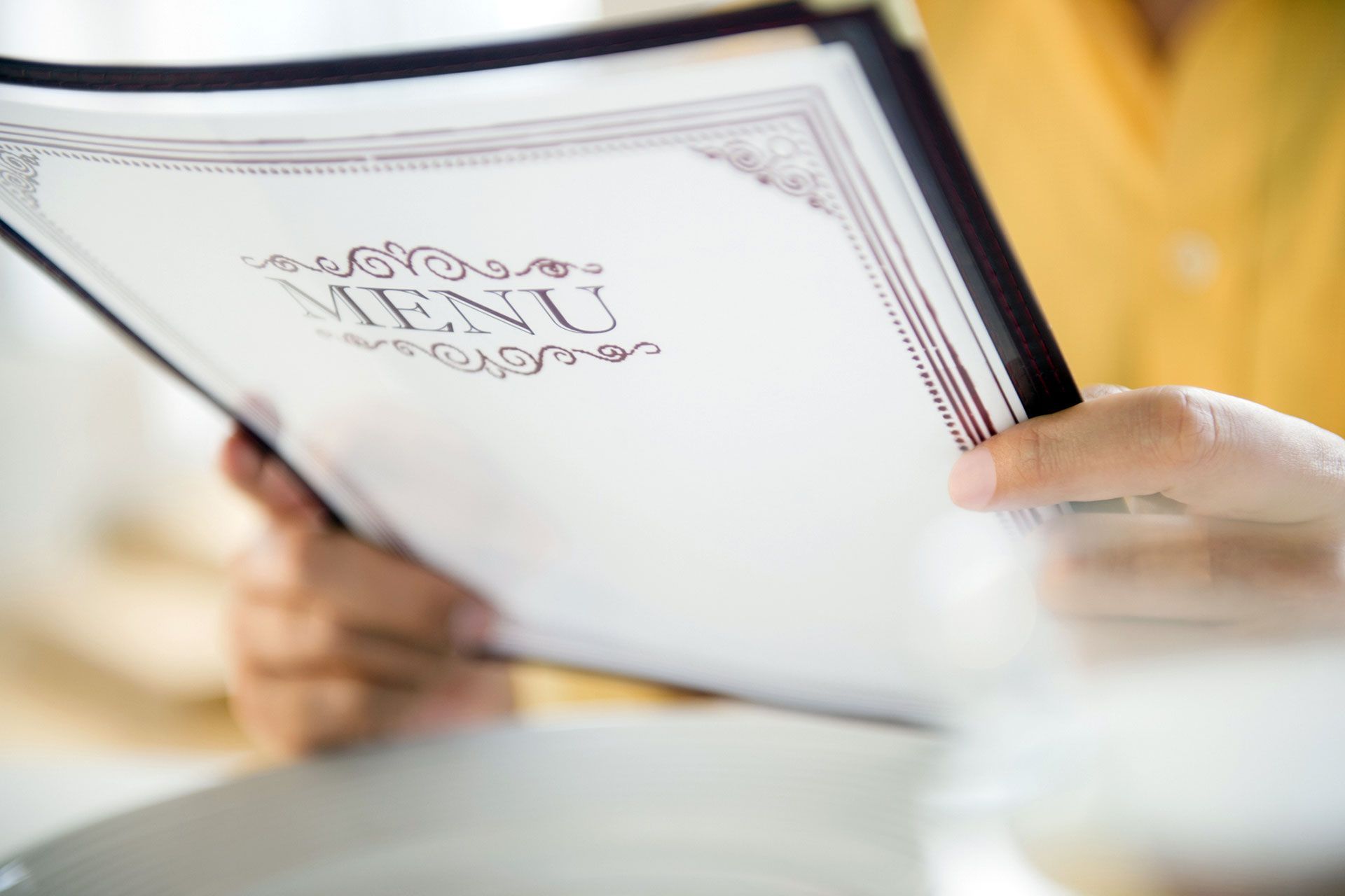 Persona che tiene in mano il menù di un ristorante e legge; messa a fuoco morbida, colori caldi.