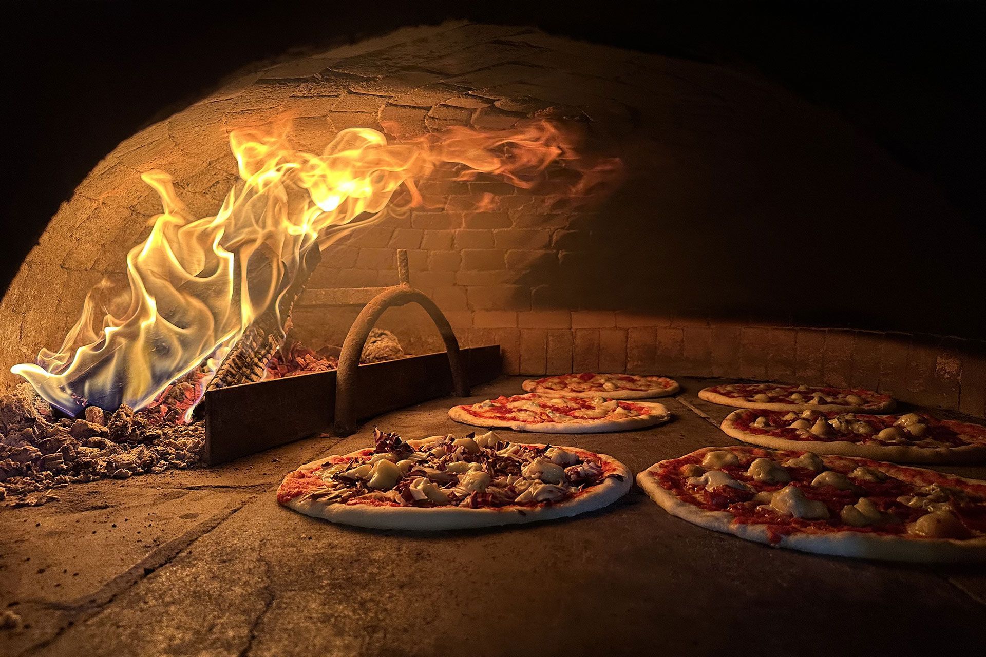 Pizze cotte nel forno a legna con fiamma, con interno in mattoni e condimenti a vista.