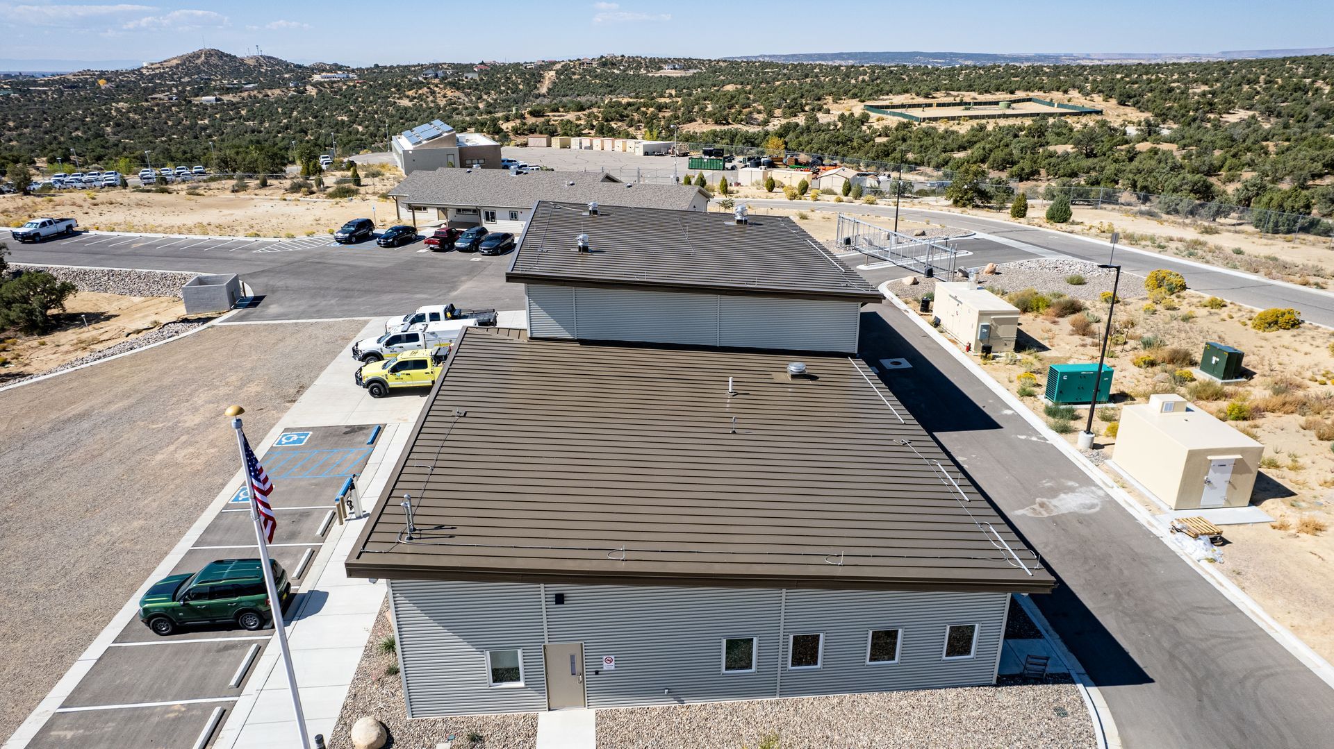 Aerial view along the dark metal roof panels of a gray fire station with rooftop vents.