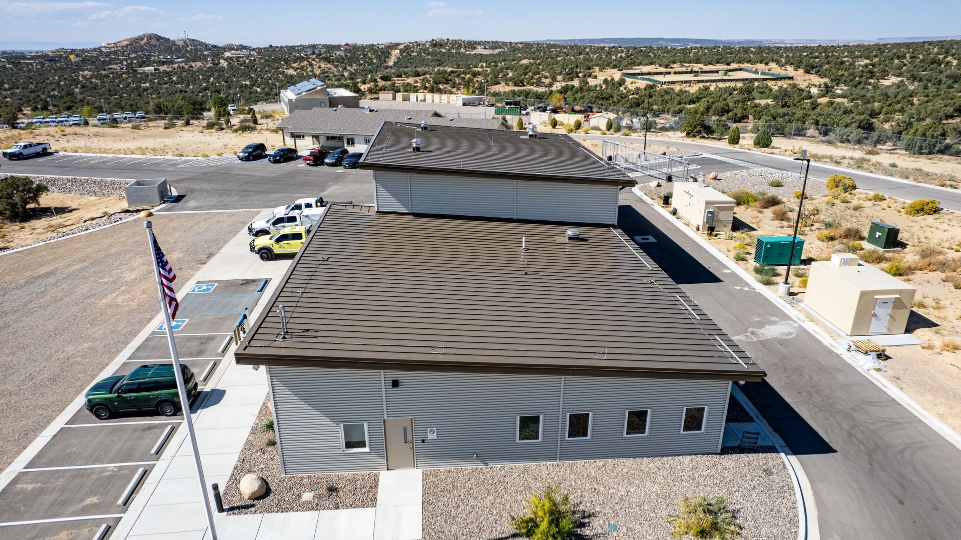 Elevated rear view of a gray fire station with dark metal roof sections and rectangular windows.