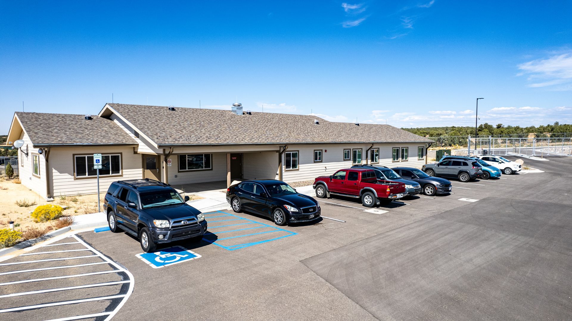 Front view of a beige single-story building with a shingle roof and vehicles in marked parking spaces.