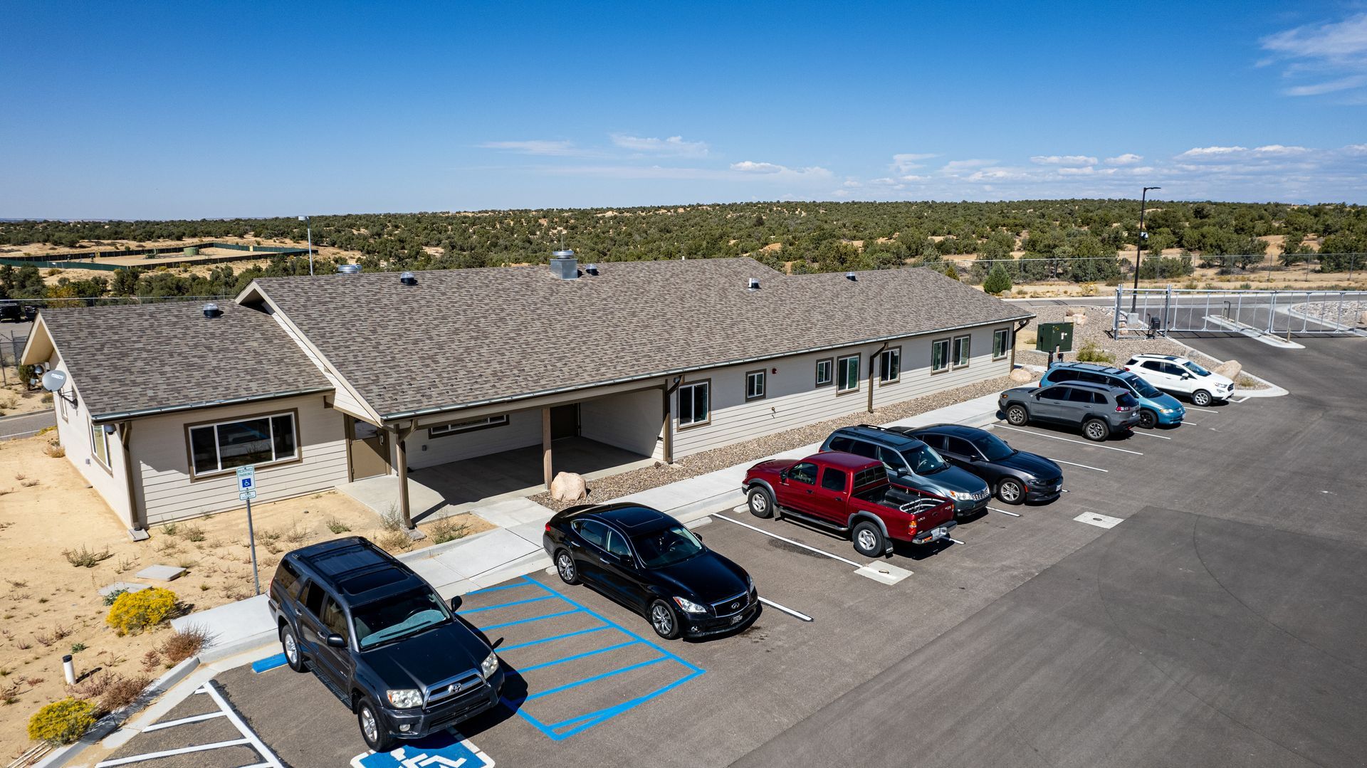 Angled aerial view of a beige building with a gray shingle roof, rooftop vents and a parking lot.