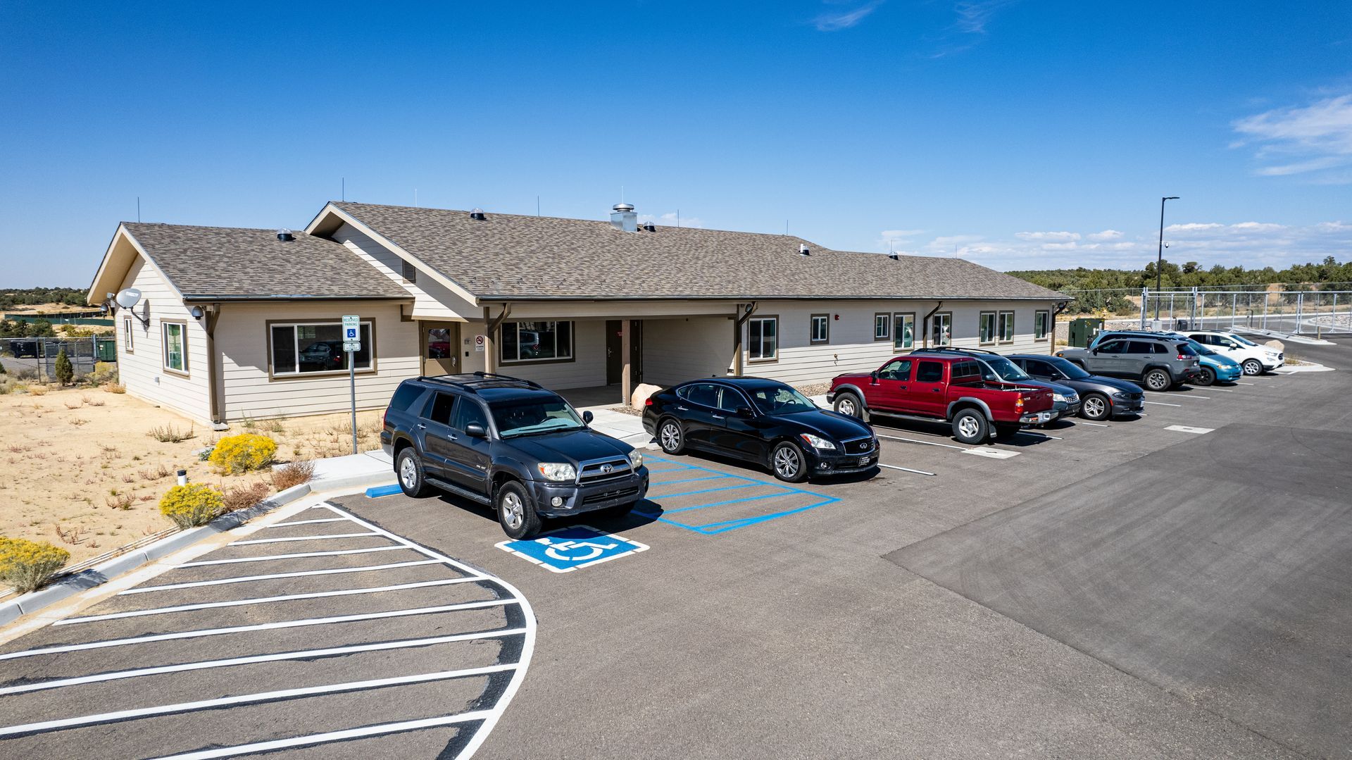 Front corner view of a beige building with a gray shingle roof and accessible parking spaces.