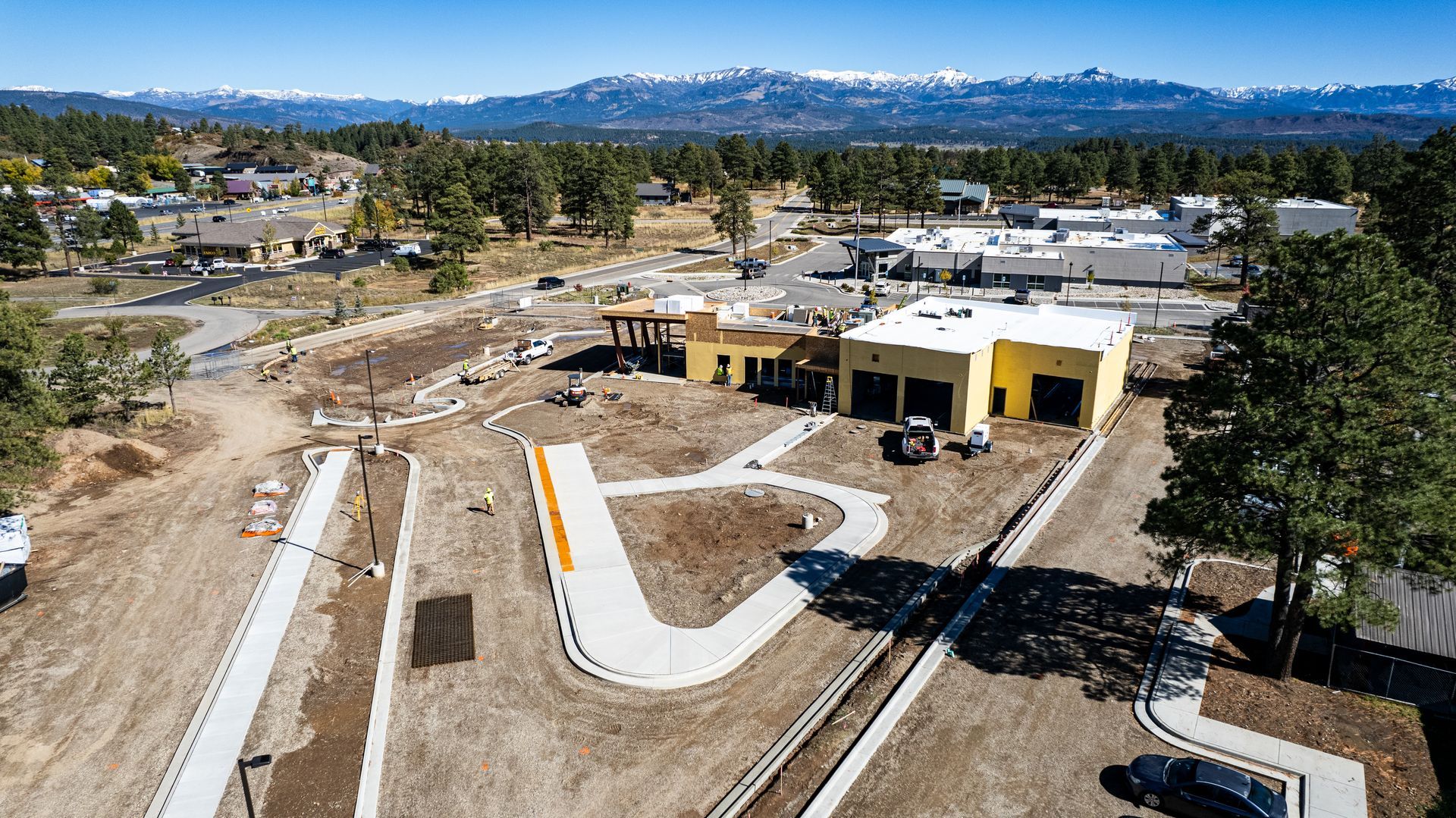 Aerial view of a building under construction with yellow wall sheathing, a white low-slope roof and mountains in the distance.